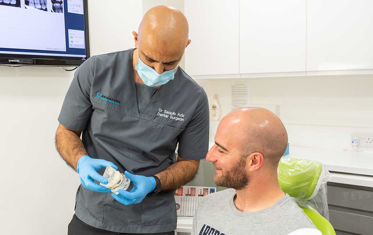 A smiling patient at a dental appointment with a dentist holding a teeth mould