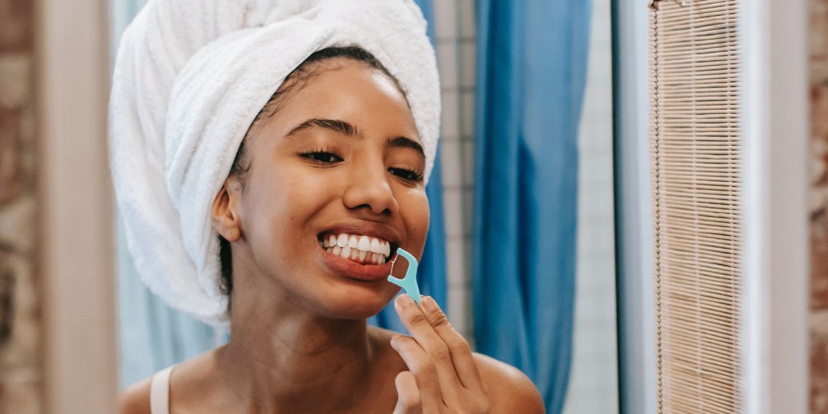 Woman flossing her teeth in front of a mirror, keeping her teeth and gums healthy